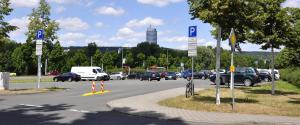 Blick auf den Seidelparkplatz in Jena im Vordergrunddie EInmündung, Bäume einzenlne Fahrzeuge, im Hintergrund ist der Uniturm zu sehen.