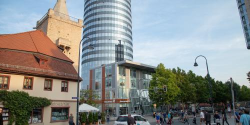 Blick vom Johannisplatz in Richtung Neue Mitte Jena und den Leutragraben, zu sehen sind Fußgänger, die die Straße queren und Fahrradfaher und Autos