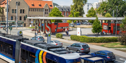 Im Vordergrund eine Straßenbahm im Hinergrund rechts Autos auf der Weigelstraße und der Busbahnhof, im Hintergrund oberhalb der Straßenbahn das Volkshaus Jena